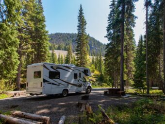 Beautiful campsite in the mountains with an RV and wooden bench. beautiful campsite mountains with rv wooden bench scaled