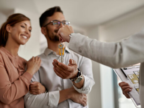 Close-up of real estate agent giving new house keys to a couple. closeup real estate agent giving couple keys their new home scaled