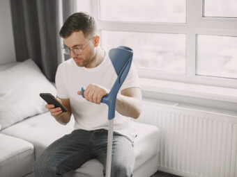 Young man with walking stick talk by phone indoors young man with broken leg home using smartphone scaled