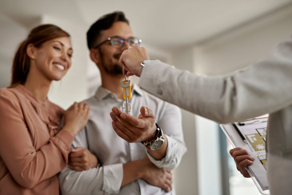 closeup real estate agent giving couple keys their new home scaled