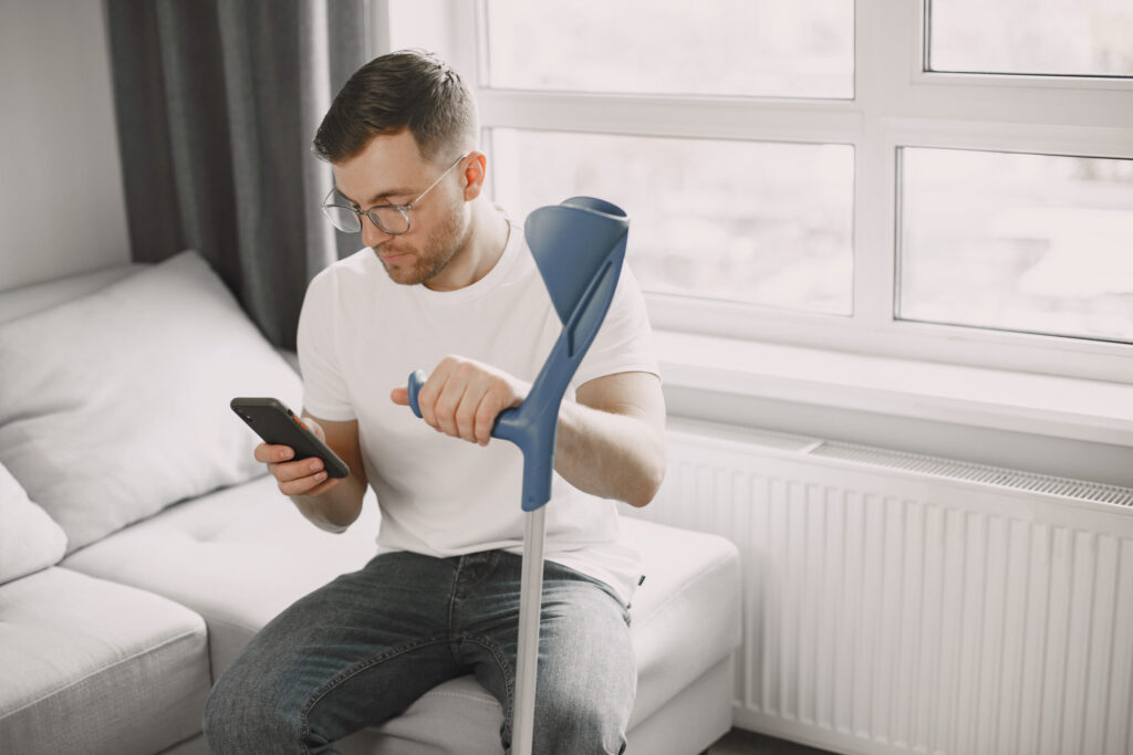 young man with broken leg home using smartphone scaled